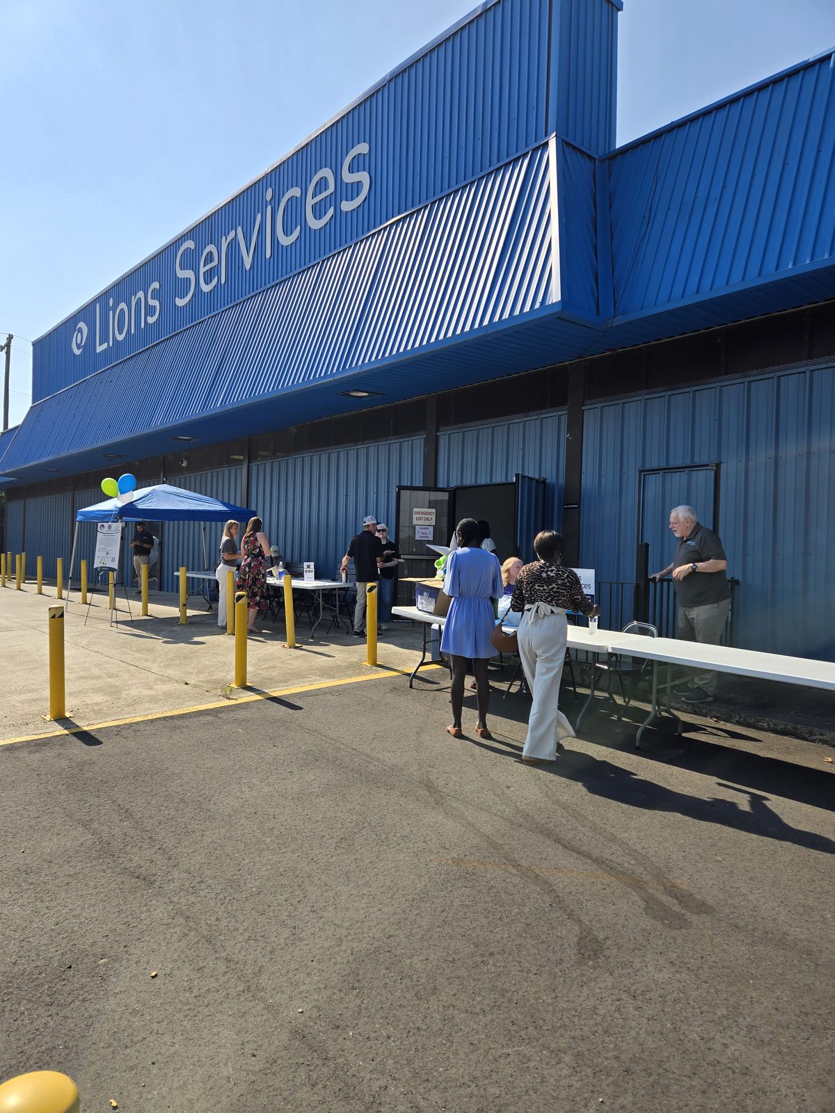 Guests gather outside the Lions Services building in Charlotte for the Braille Trail reveal, beneath the large blue 
