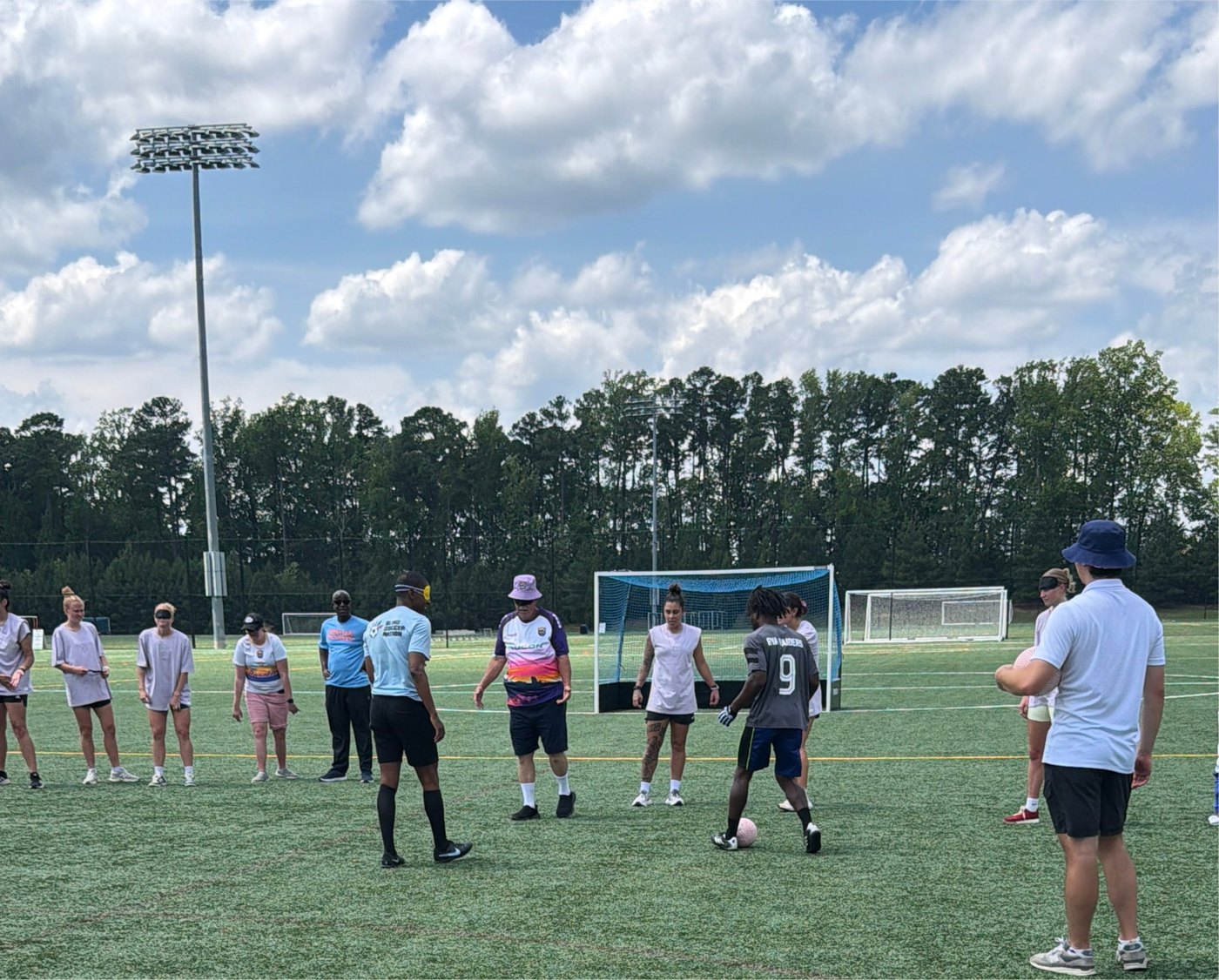 Athletes and coaches form a circle on the soccer field as a player dribbles near the goal during the Blind Soccer Expo.
