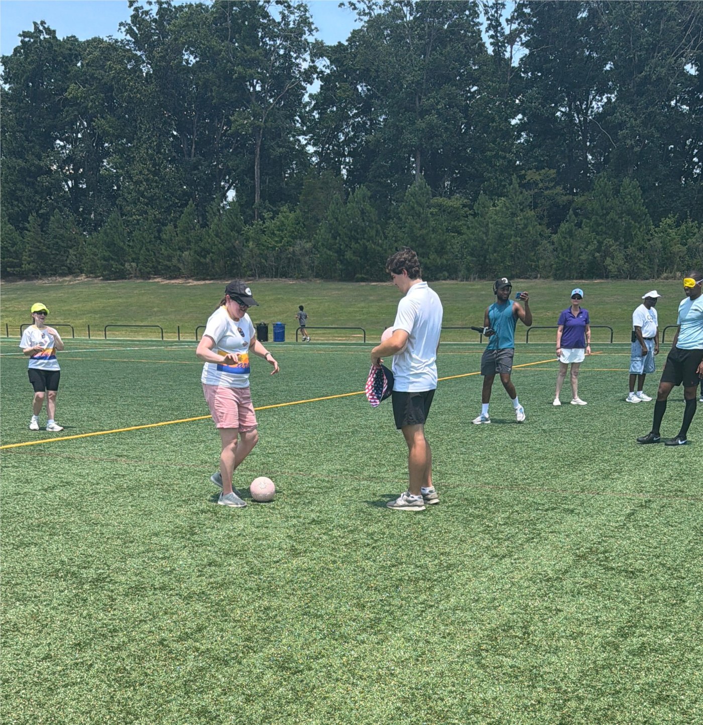Two participants practice with a soccer ball on green turf while others look on during the Blind Soccer Expo.