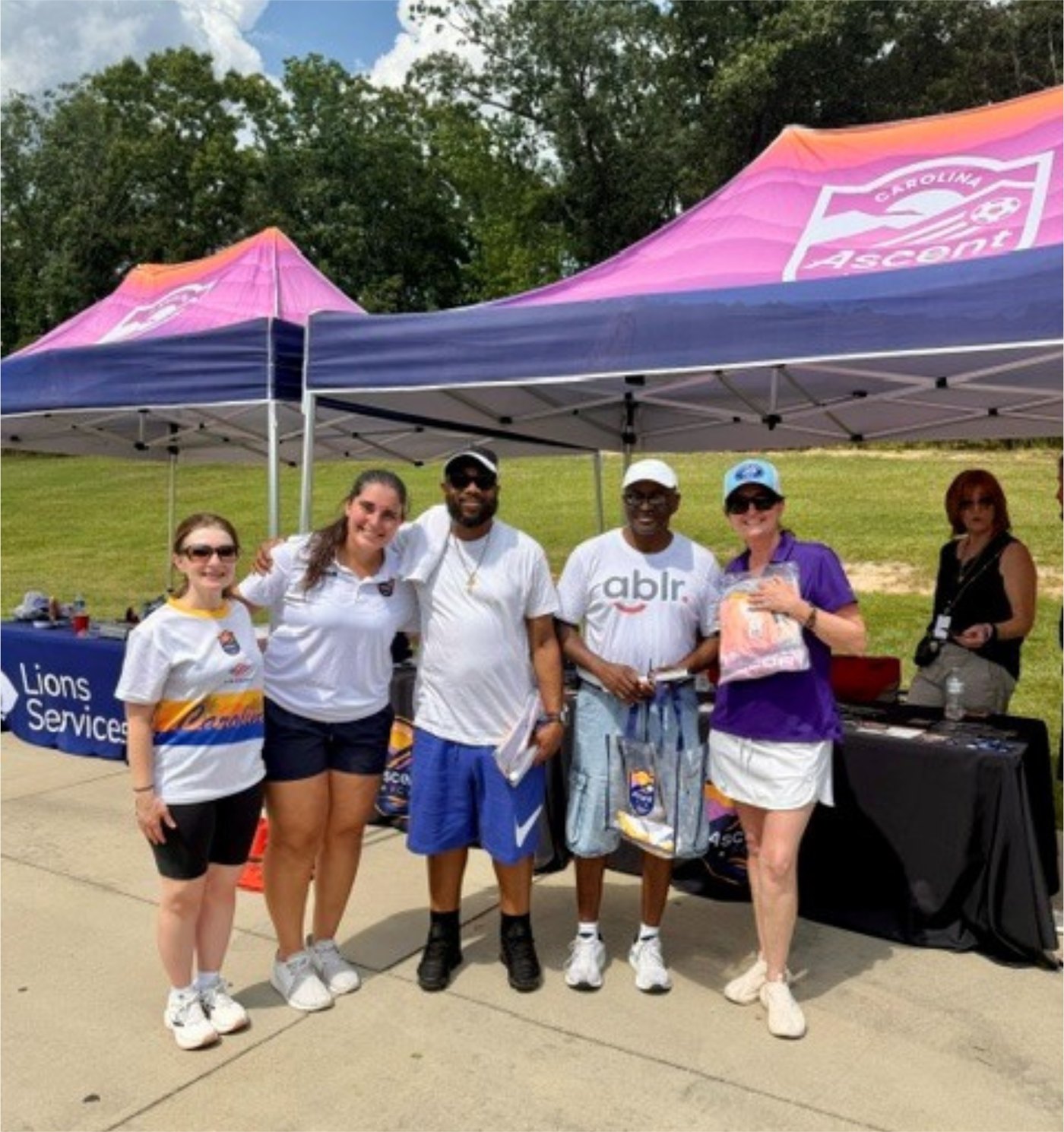 Volunteers and partners smile under a Carolina Ascent tent beside a Lions Services table at the Blind Soccer Expo.