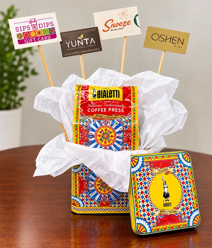 Decorative tin holding a Bialetti coffee press, with gift cards for four Charlotte restaurants displayed on picks above it.